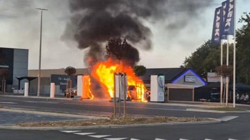 Un véhicule électrique en flammes à proximité d'une borne de recharge, illustrant un incident d'incendie.